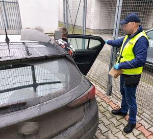 Policjant w żółtej kamizelce prowadzi zatrzymanego mężczyznę