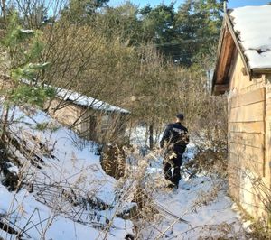 Policjant idzie w stronę pustostanów, ziemia pokryta jest śniegiem.