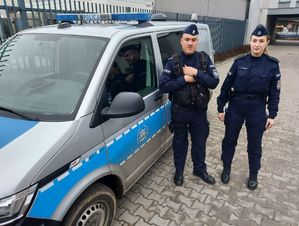 Policjant i policjantka stoją przy radiowozie.