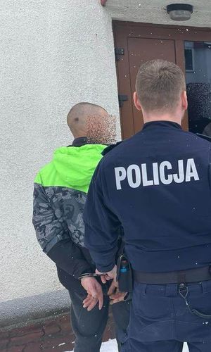 Policjant prowadzi zatrzymanego mężczyznę.