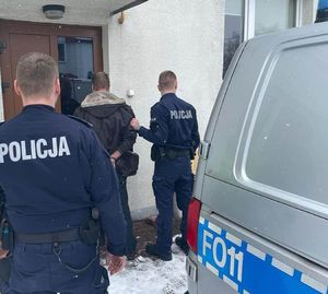 Dwóch policjantów prowadzi w środku zatrzymanego mężczyznę.