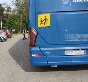 Policjant w żółtej kamizelce z napisem policja i białej czapce stoi przy dużym autobusie szkolnym