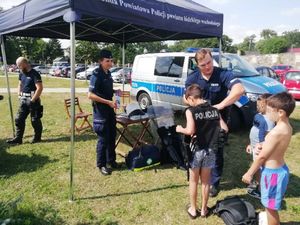 Policjant i policjantka stoją przy radiowozach a przy nich stoją dzieci.