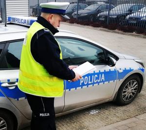 Policjant w żółtej kamizelce stoi przy radiowozie.