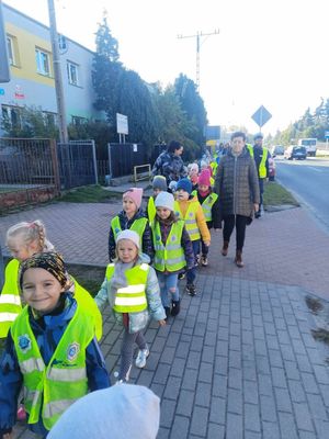 Policjanci stoją na drodze przez którą przechodzą dzieci w odblaskowych kamizelkach.