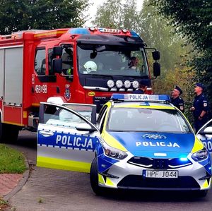 Policjanci stoją obok radiowozu i przy wozie strażackim/.