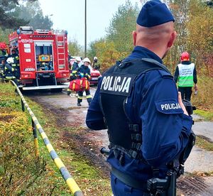 Policjant stoi i patrzy w stronę wozu strażackiego.