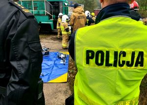 Policjant w żółtej kamizelce stoi przy strażakach.