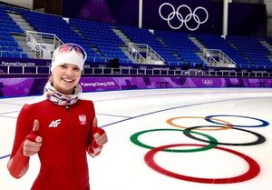 Łyżwiarka stoi na torze lodowym z symbolem 5 kółek olimpijskich.