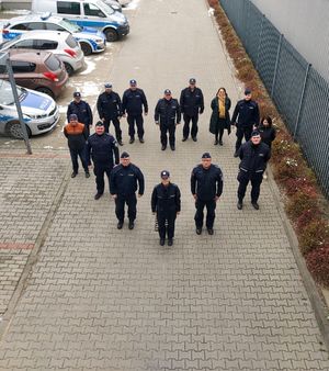 Policjanci i pracownicy stoją na placu wewnętrznym, są ustawieni w kształcie serca, obok stoją radiowozy.