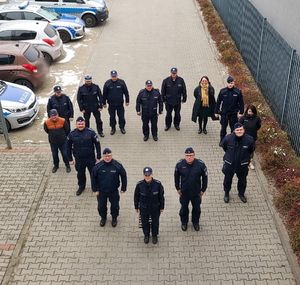 Policjanci i pracownicy stoją na placu wewnętrznym, są ustawieni w kształcie serca, obok stoją radiowozy.