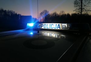 Sygnalizator świetlny na dachu radiowozu z napisem policja, migają światła niebieskie.