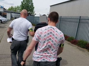 Dwóch policjantów z opaskami na przedramieniu z napisem policja prowadzi zatrzymanego mężczyznę.