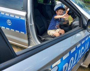 Mały chłopiec w białej policyjnej czapce siedzi w radiowozie i się uśmiecha.