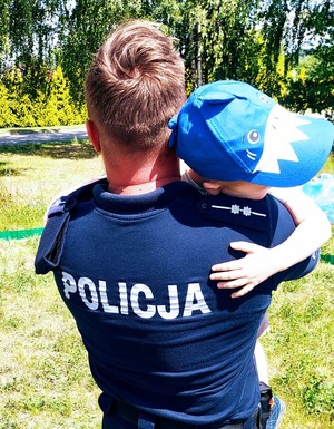 Mały chłopiec przytula się do policjanta, który trzyma go w ramionach.