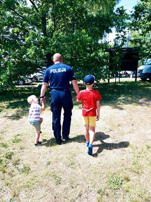 Policjant idzie przed siebie, trzyma za rękę dwóch małych chłopców.