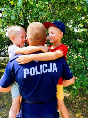 Policjant trzyma na rękach dwóch małych chłopców, którzy go obejmują.