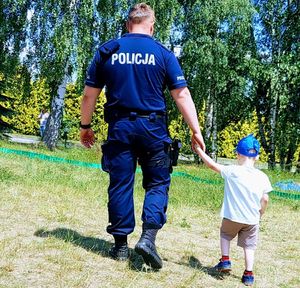 Policjant idzie przed siebie a za rękę prowadzi małego chłopca.
