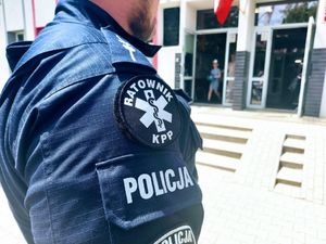 Policjant w mundurze z naszywką z napisem policja ratownik stoi przed budynkiem szkoły.