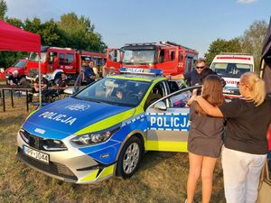 Policjantki i policjanci stoją przy granatowym namiocie, radiowozie i motocyklach i rozmawiają z ludźmi.