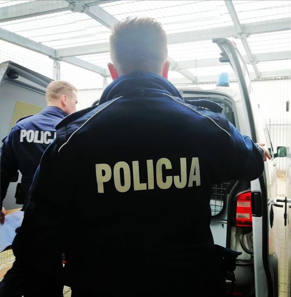 Dwóch policjantów zamyka tylne drzwi radiowozu.