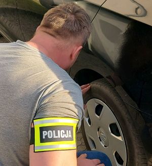 Policjant z opaską na ramieniu z napisem policja sprawdza opony w samochodzie.