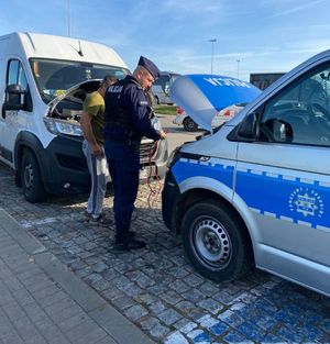 Policjant stoi przy radiowozie a przed nim stoi biały bus.