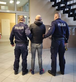 Dwóch policjantów prowadzi w środku zatrzymanego mężczyznę.