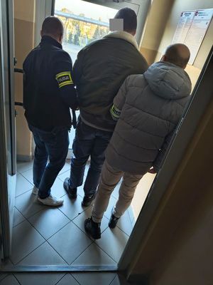 Dwóch policjantów prowadzi w środku zatrzymanego mężczyznę.