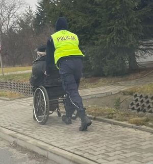 Policjantka prowadzi wózek inwalidzki z mężczyzną.