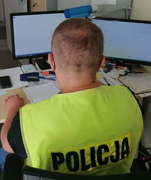 Policjant w żółtej kamizelce z napisem policja siedzi przy biurku.