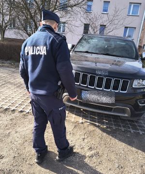 Policjant stoi przy zaparkowanym czarnym samochodzie.