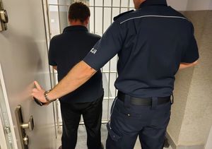 Policjant stoi obok zatrzymanego mężczyzny.