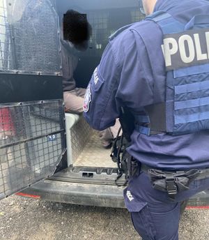 Policjant stoi przy radiowozie, w którym siedzi poszukiwany mężczyzna.