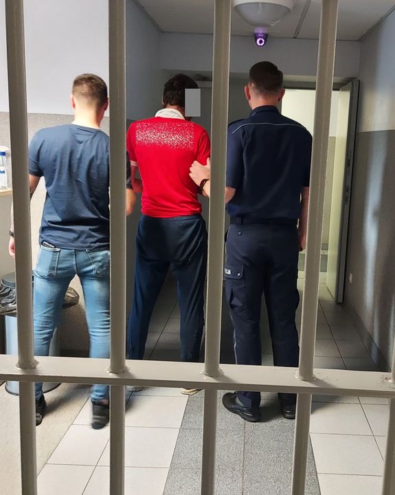 Dwóch policjantów stoi obok zatrzymanego mężczyzny w środku.