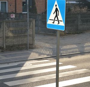 Przejście dla pieszych, obok stoi znak drogowy.