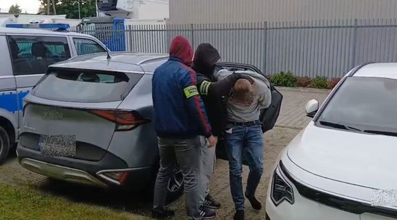 Dwóch policjantów prowadzi zatrzymanego mężczyznę.