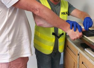 Policjant pobiera odciski palców zatrzymanemu mężczyźnie.