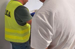 Policjant pobiera odciski palców zatrzymanemu mężczyźnie.