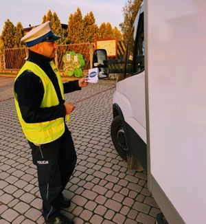 Policjant wręcza ulotki z napisem Mistrzu zwolnij kierującym autami.