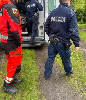 Policjanci stoją przy karetce pogotowia, obok nich ratownik medyczny.