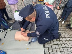 Policjanci prowadzą pokaz akcji resuscytacyjnej, obok nich są dzieci.