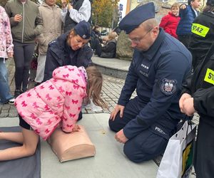 Policjanci prowadzą pokaz akcji resuscytacyjnej, obok nich są dzieci.