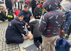 Policjanci prowadzą pokaz akcji resuscytacyjnej, obok nich są dzieci.