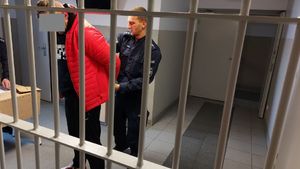 Policjant zapina kajdanki na ręce zatrzymanemu mężczyźnie.