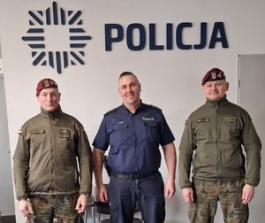 Policjant i funkcjonariusze wojska stoją ustawieni do zdjęcia, nad nimi jest napis Policja.