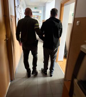 Policjant prowadzi zatrzymanego mężczyznę.