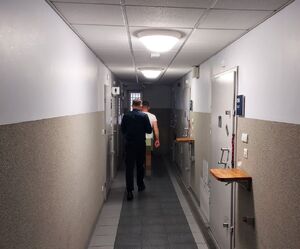 Policjant prowadzi zatrzymanego mężczyznę korytarzem.