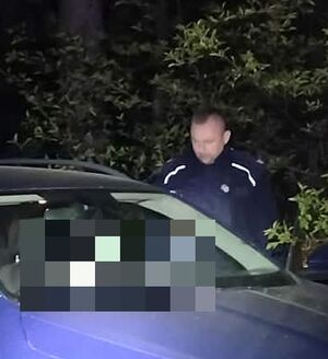 Policjant stoi przy odnalezionym mężczyźnie w samochodzie.