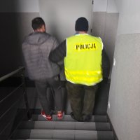 Policjant prowadzi zatrzymanego mężczyznę.
